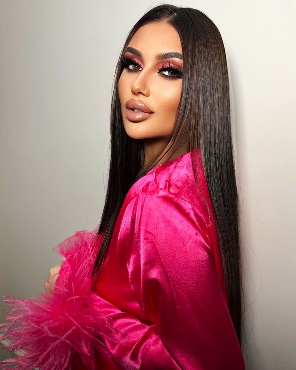 Dominica with long straight dark hair wears a pink satin top with feathered sleeves against a plain light background.